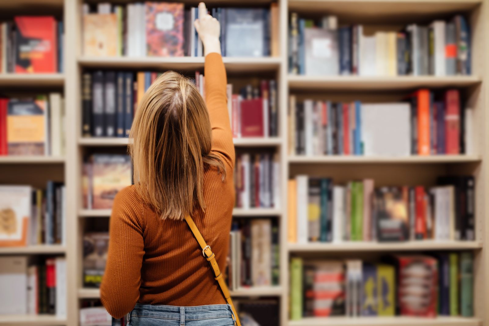 person reaching for books on bookshelf